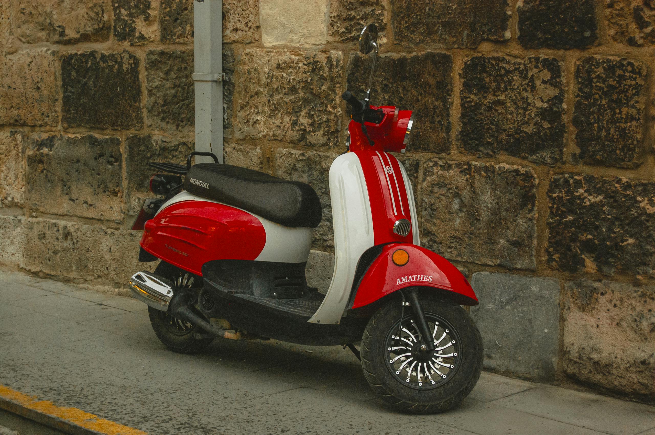Classic red and white scooter parked against a rustic stone wall in Konya, Türkiye.